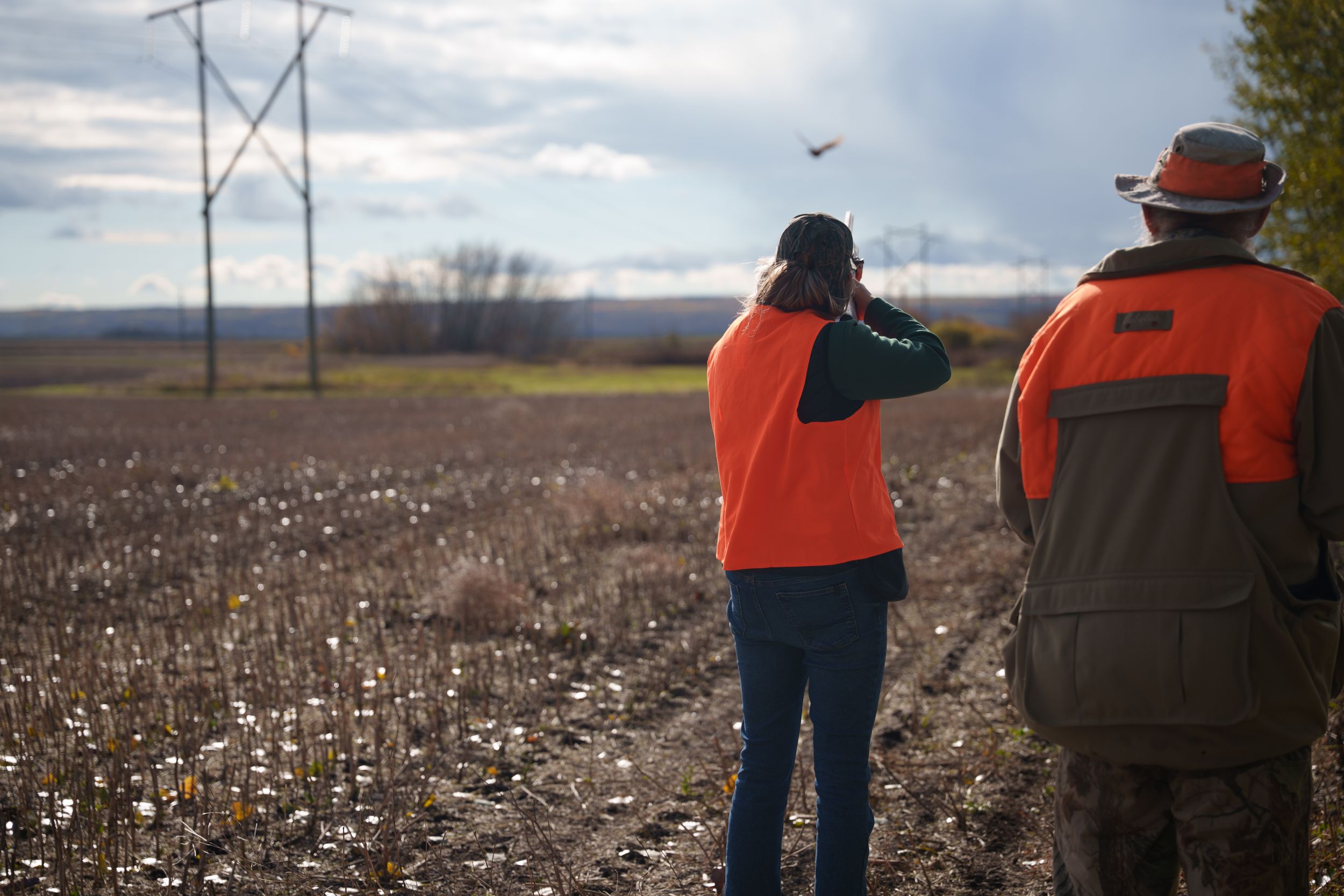Group of hunters walking through a harvested cotton field with scattered white cotton bolls visible on the ground.
