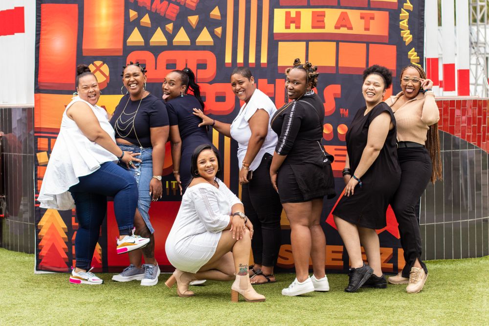 Group posing together against colorful geometric wall art at outdoor event.