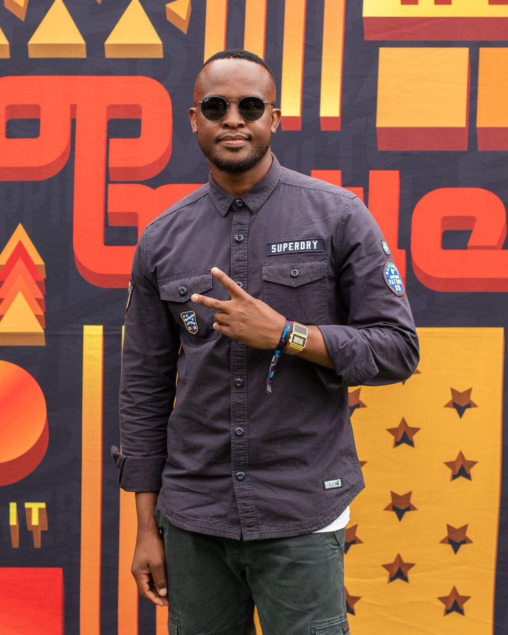 Person in sunglasses and dark shirt poses in front of geometric patterned wall.