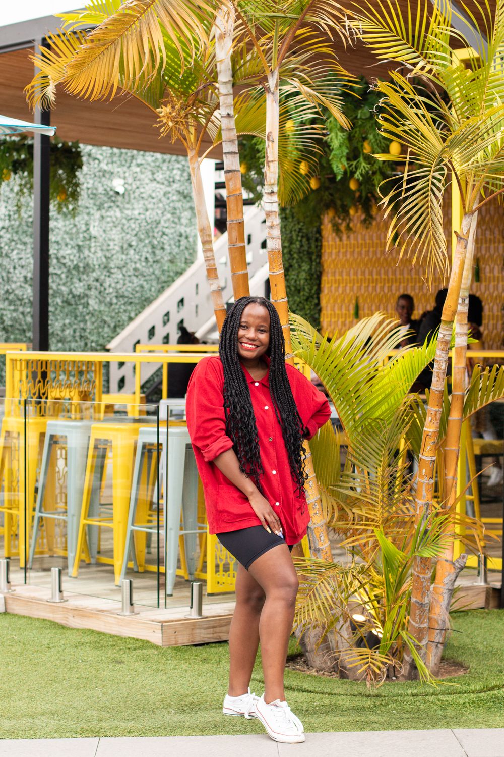 Person in red sweater poses near tropical palm trees in outdoor venue setting.