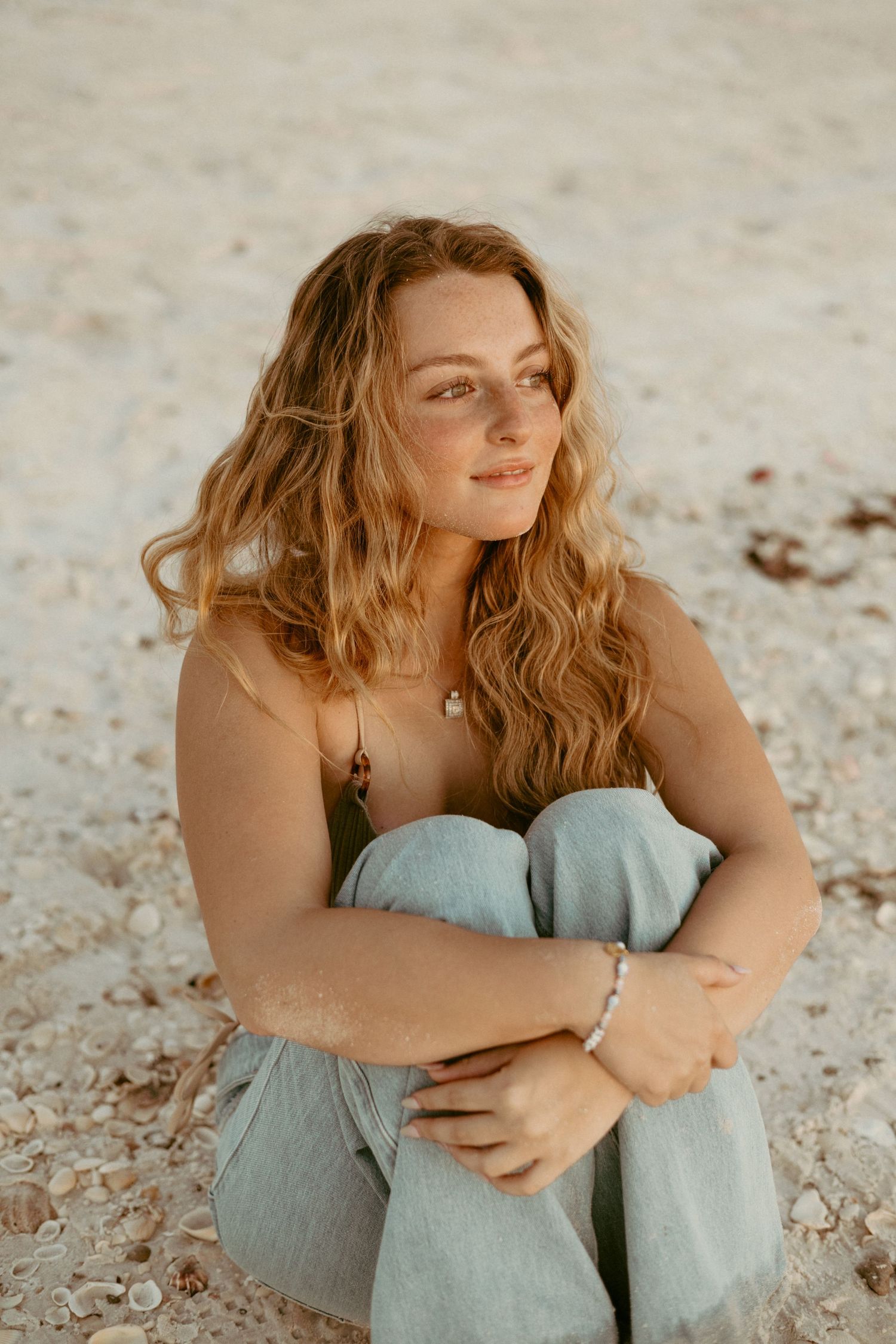 girl looking off into distance with jeans on the sand