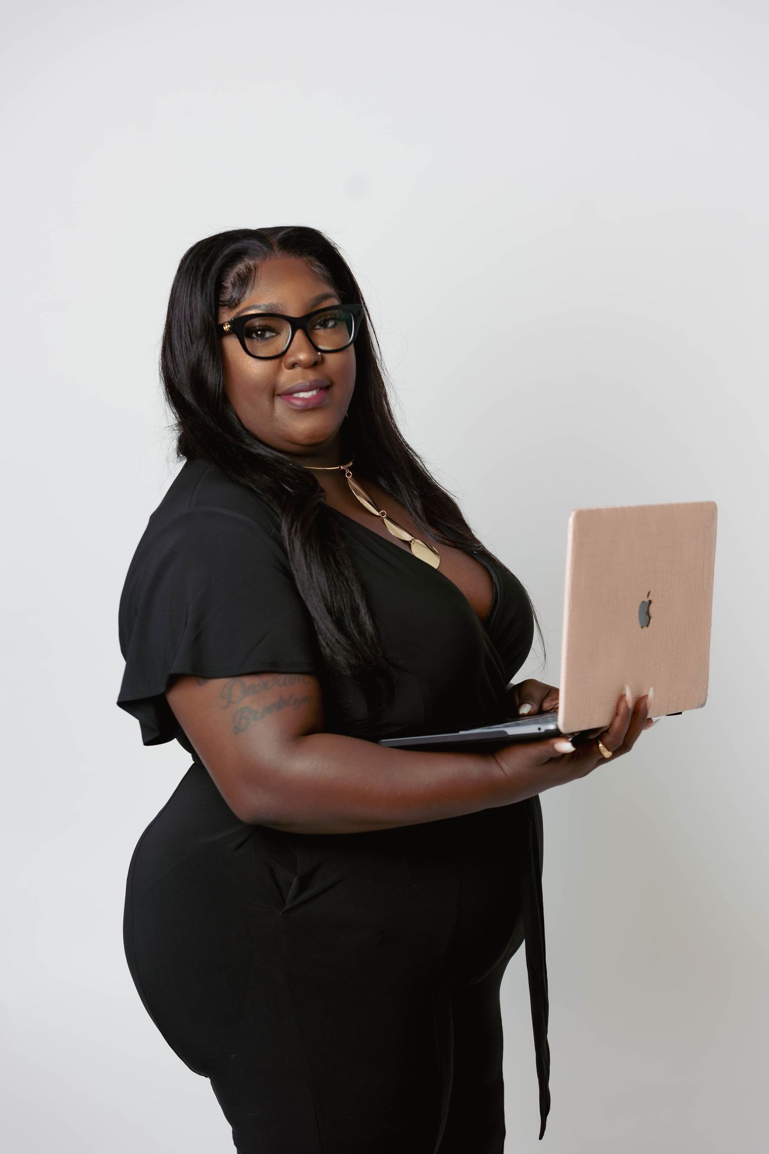 Professional woman in black dress holding a rose gold MacBook laptop against white background.