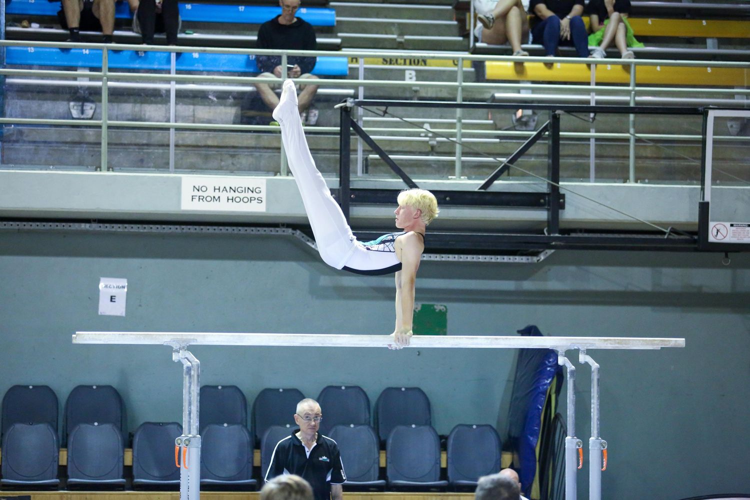 Gymnast performs inverted handstand on parallel bars in indoor arena.