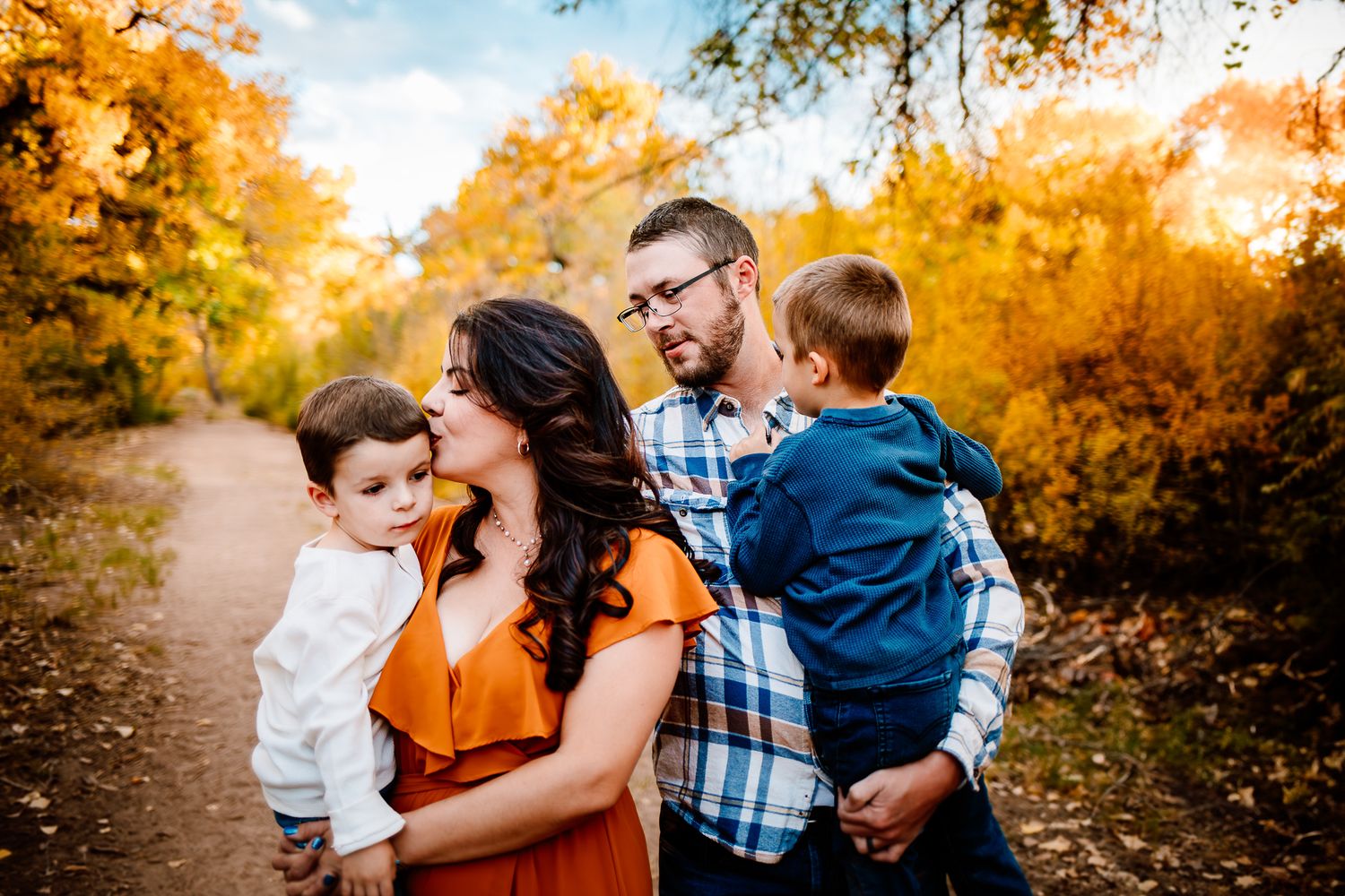 A family portrait captured during golden hour among fall foliage on a walking path.