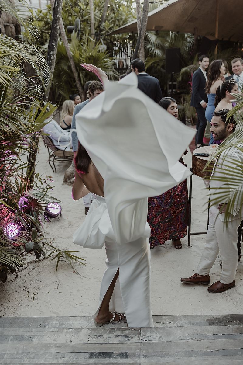 Bride in white gown dancing at outdoor tropical wedding reception with guests watching.