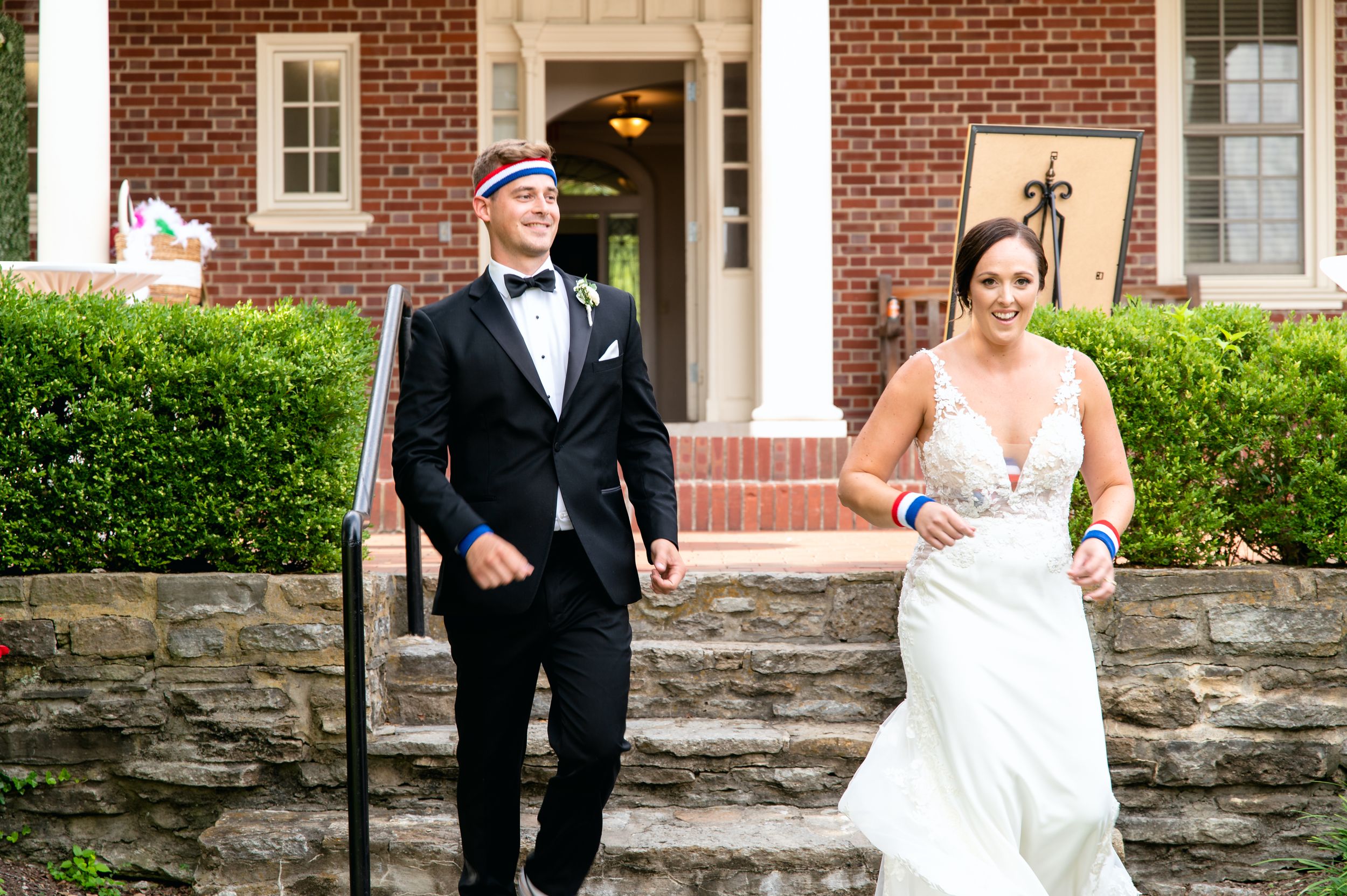 Bride in white gown and groom in black tuxedo walking hand in hand outside a brick building on their wedding day.