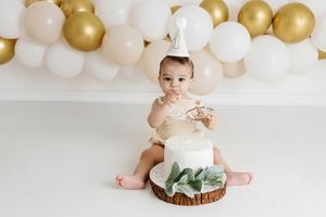 Baby in a beige onesie and party hat eating cake by 1st birthday photographer in Menifee.