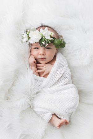 Portrait of cute newborn baby girl wrapped in white knit blanket.