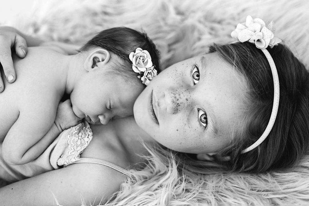 Menifee California newborn baby photographer black and white portrait of a big sister with freckles holding her baby sister.