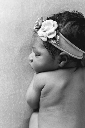 Black and white profile portrait of sleeping newborn baby girl wearing a floral headband.