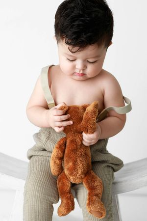 Cute baby boy sitting and holding a brown teddy bear by timeless classic baby photographer in Menifee.