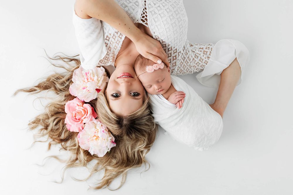 Mom with pink flowers in hair lovingly holding her newborn baby.