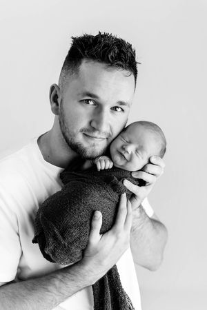 Black and white portrait of dad holding sleeping swaddled newborn baby boy.