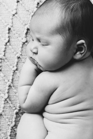 Black and white close-up of peaceful sleeping newborn baby curled up on textured blanket.