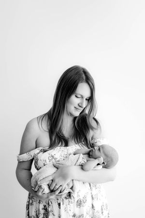 Black and white photo of a young mother tenderly cradling her newborn baby in her arms.