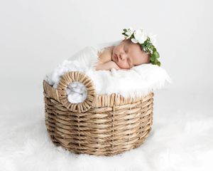 Sleeping newborn baby wearing a delicate floral crown resting in a wicker basket with white fur.