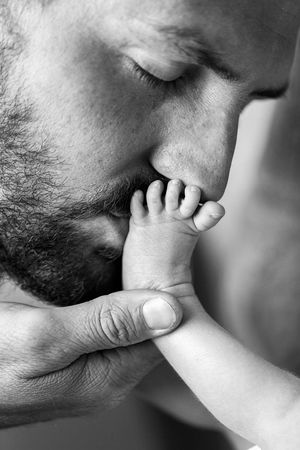 Black and white photo of a dad gently kissing his newborn baby boy's tiny foot.
