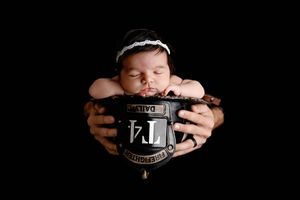 Sleeping newborn baby cradled in dad's hands holding a firefighter helmet on black background.