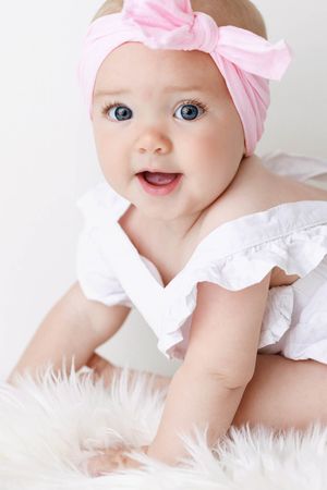 Portrait of cute baby girl with blue eyes wearing a pink bow headband.