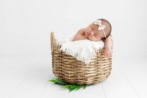 Sleeping newborn baby girl with bow headband curled up in a wicker basket with white fur lining.