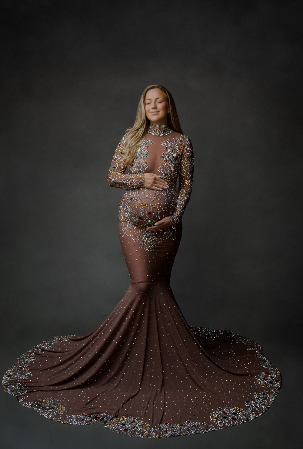 Pregnant woman in elegant floral embroidered rose gold mermaid gown with long train posing for maternity portrait.