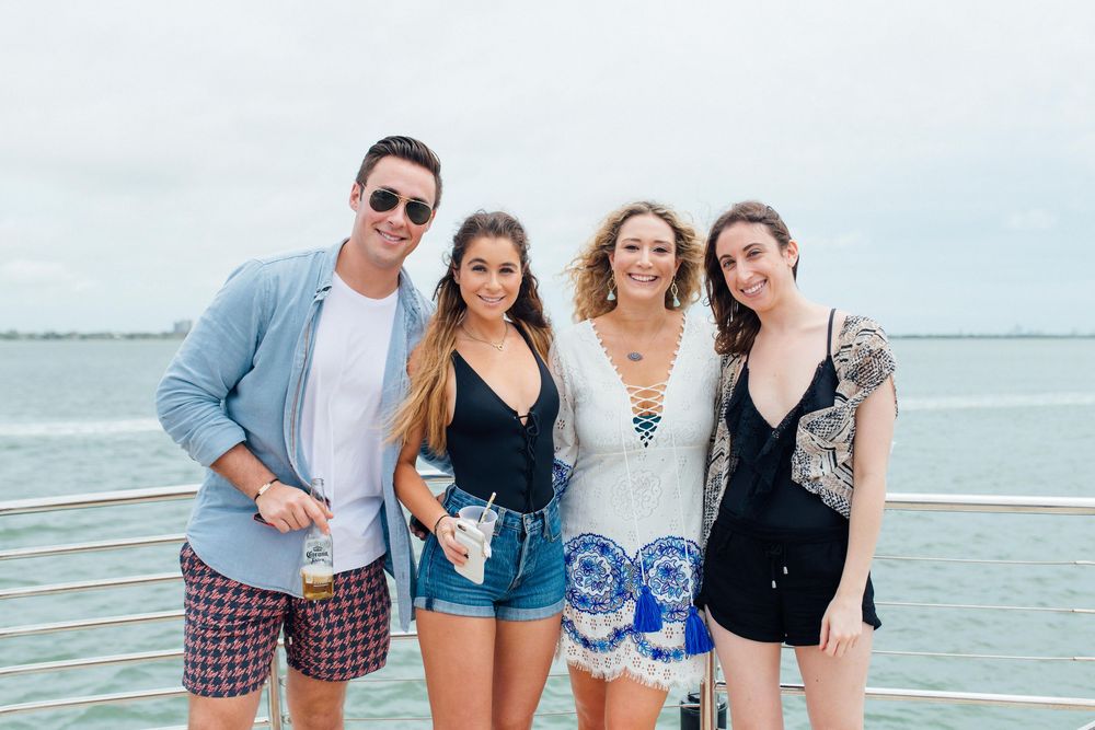 Group of four young adults smiling together on boat deck with ocean and cloudy sky behind them.