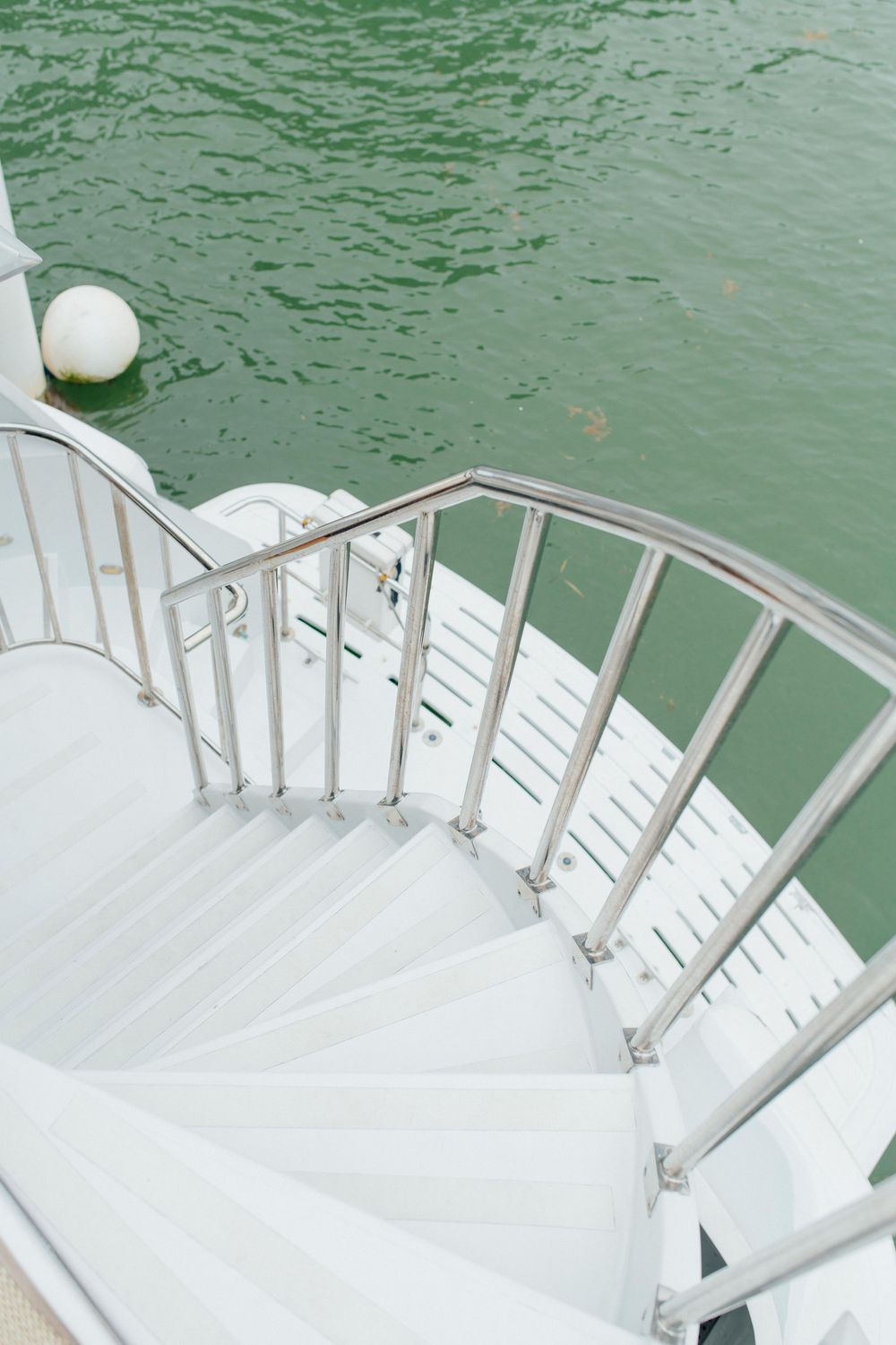 White spiral staircase with metal railing descends toward green water on a yacht.