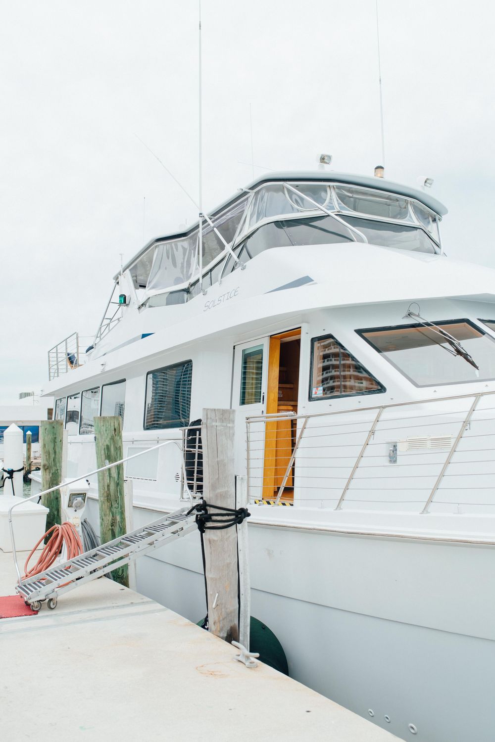 Large white luxury yacht docked at a marina pier on an overcast day.