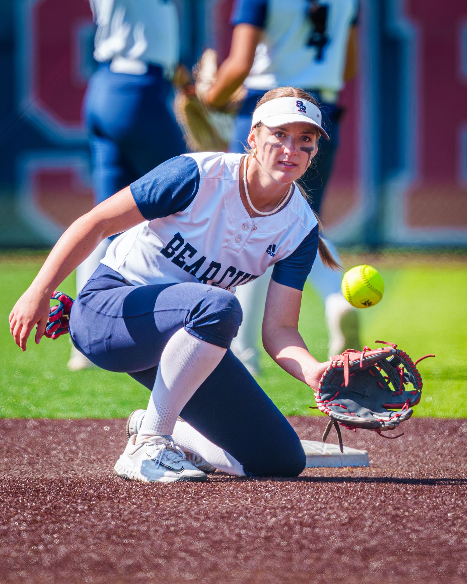 Bearcats softball player crouching low to field a ground ball during a sunny outdoor game.