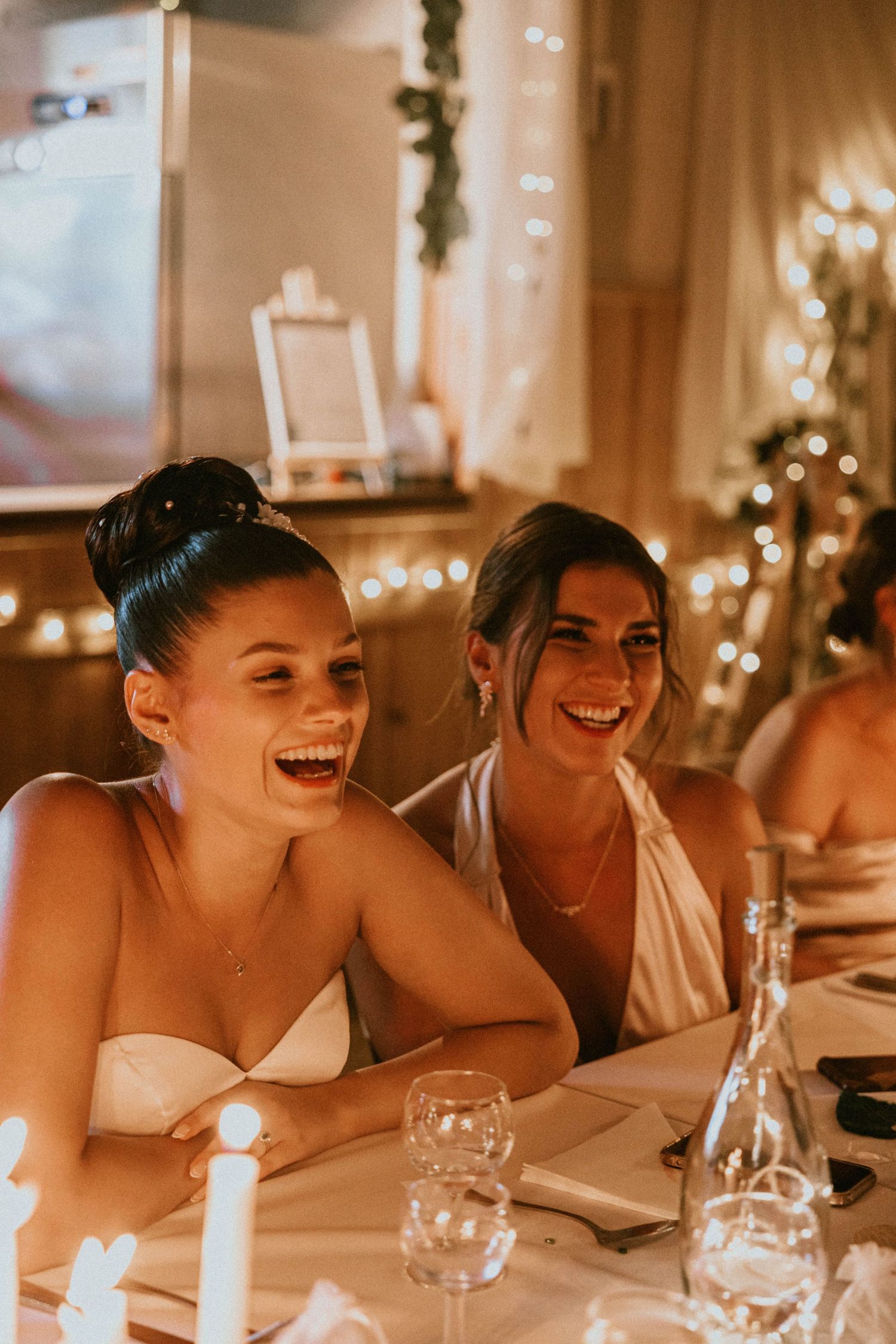 A joyful newlywed couple sits back-to-back holding chalkboard signs reading ELLE and MOI at their elegant wedding reception.