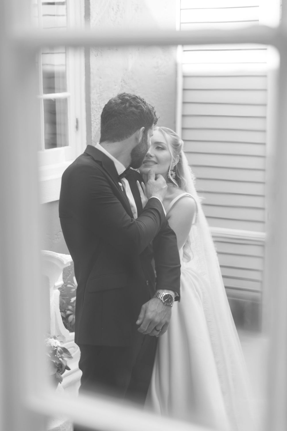 Black and white photo of a groom tenderly holding his bride's face as they share an intimate moment on their wedding day.