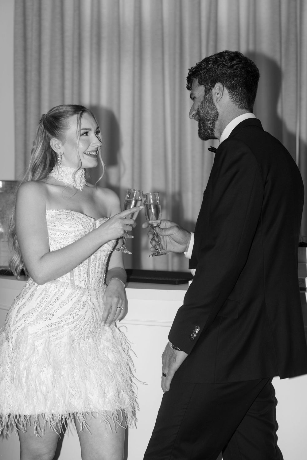 Elegant couple in formal attire toasting champagne glasses at a glamorous black and white event.