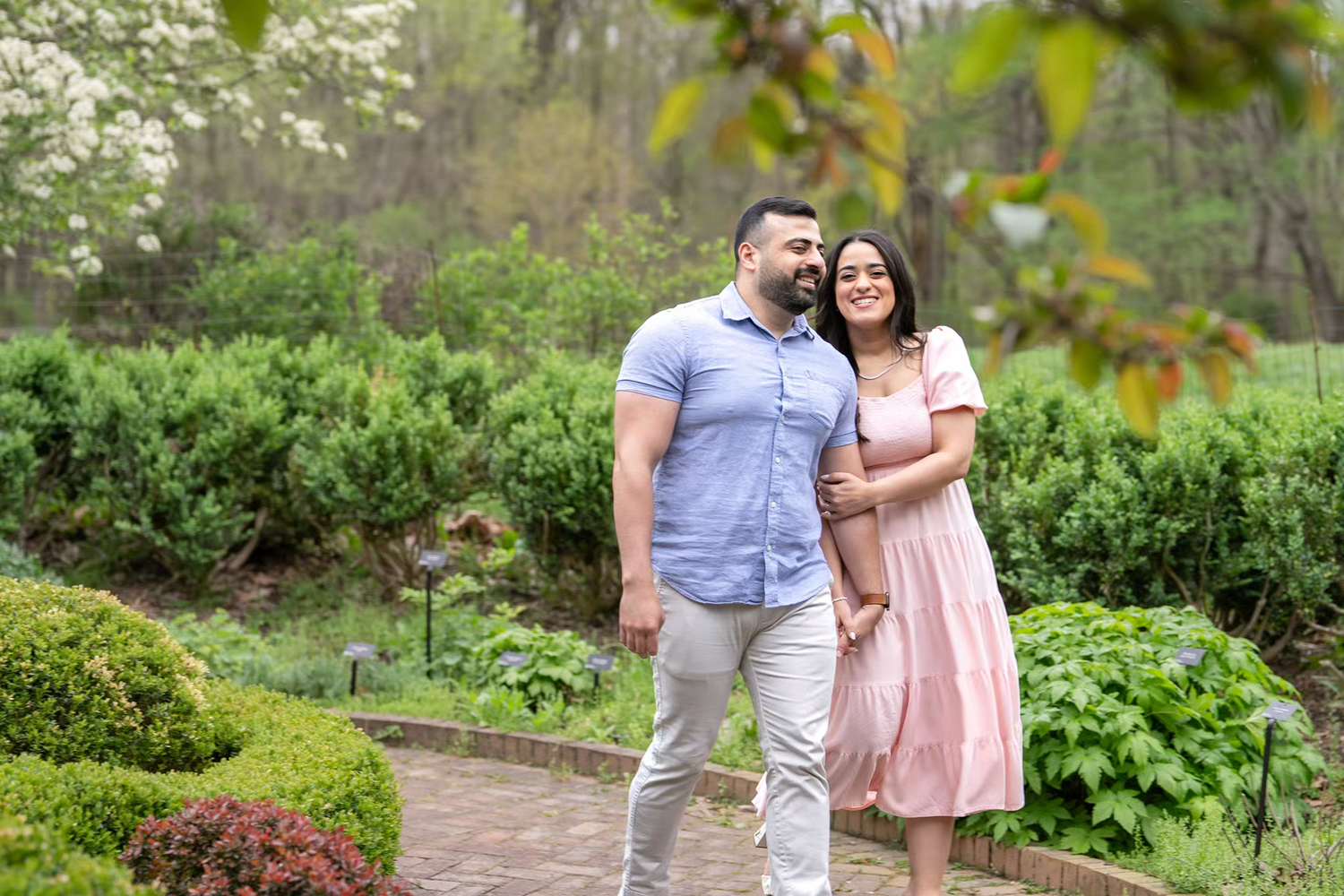 engaged couple poses together in a lush garden with blooming trees, at Inniswood Metro Gardens