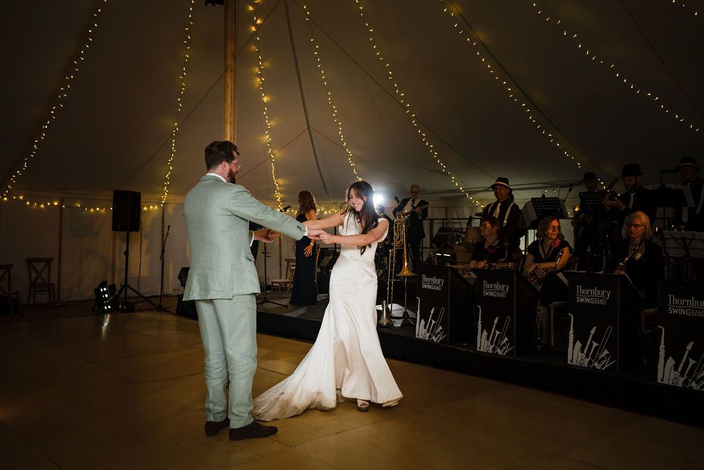 Bride and groom share first dance under twinkling lights in elegant tent with live band performing at wedding reception.