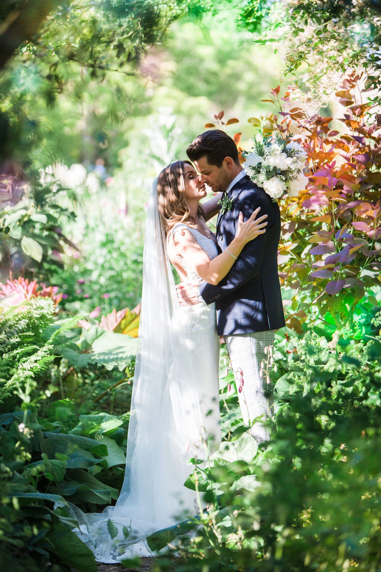 A bride and groom share a romantic moment surrounded by lush greenery and colorful flowers in the Tangled garden wedding setting.