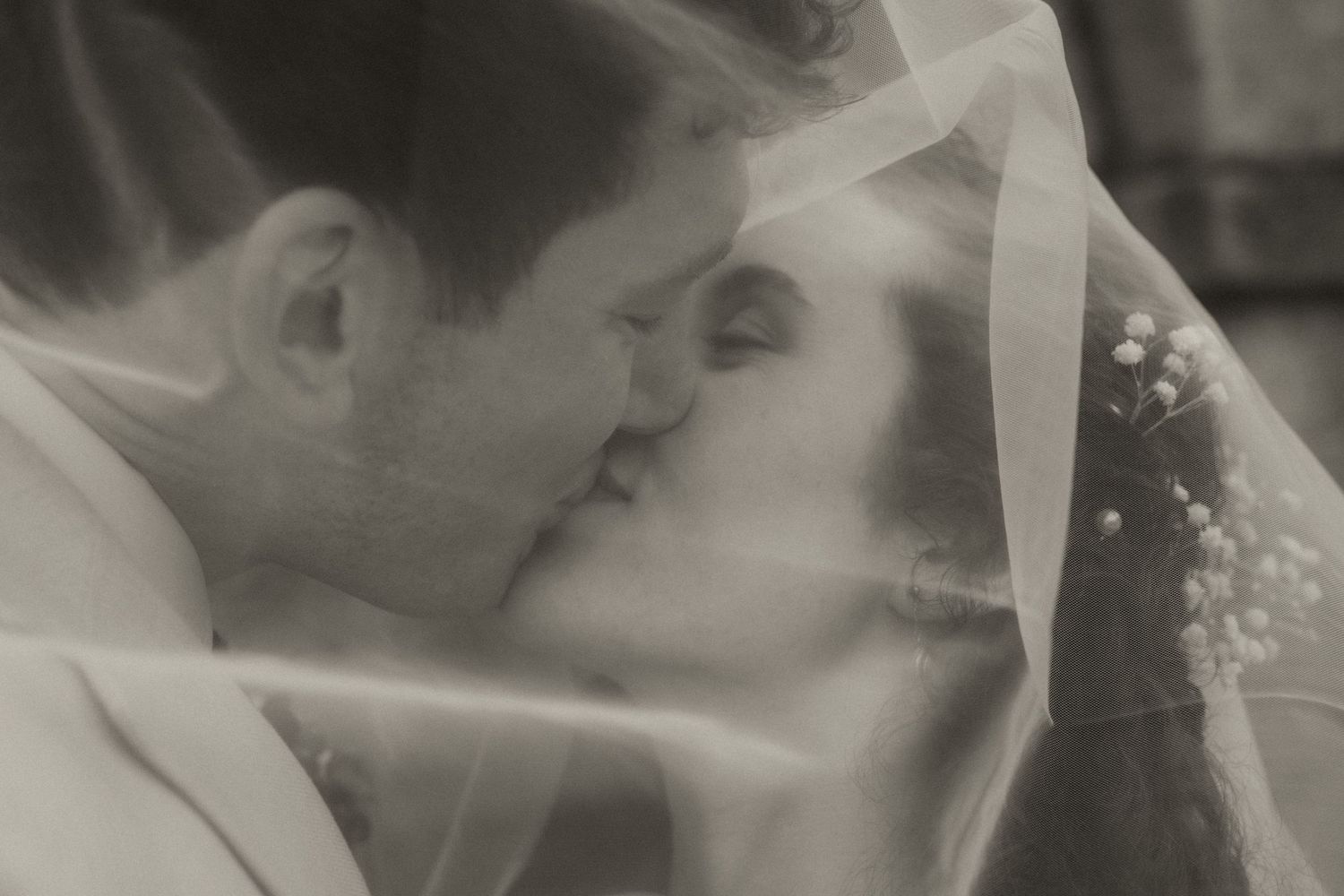 Historic stone manor house with grand entrance steps, arched doorway, symmetrical windows, and manicured hedges under a clear blue sky.