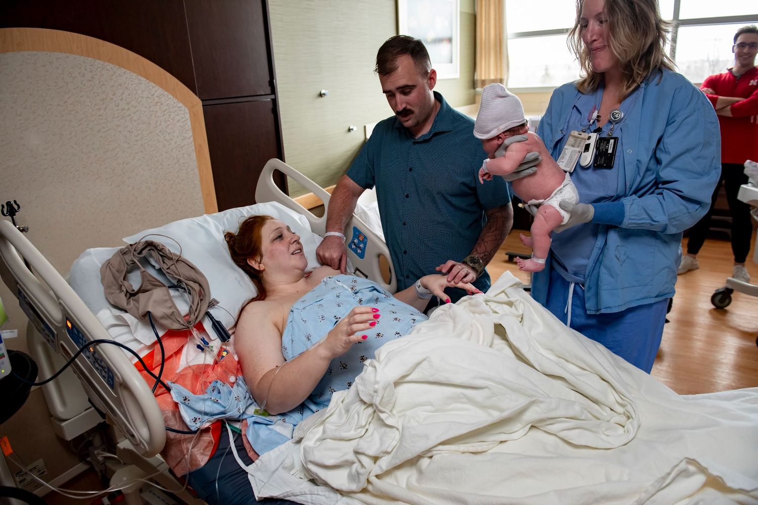 Hospital room scene shows medical staff attending to patient with newborn baby.