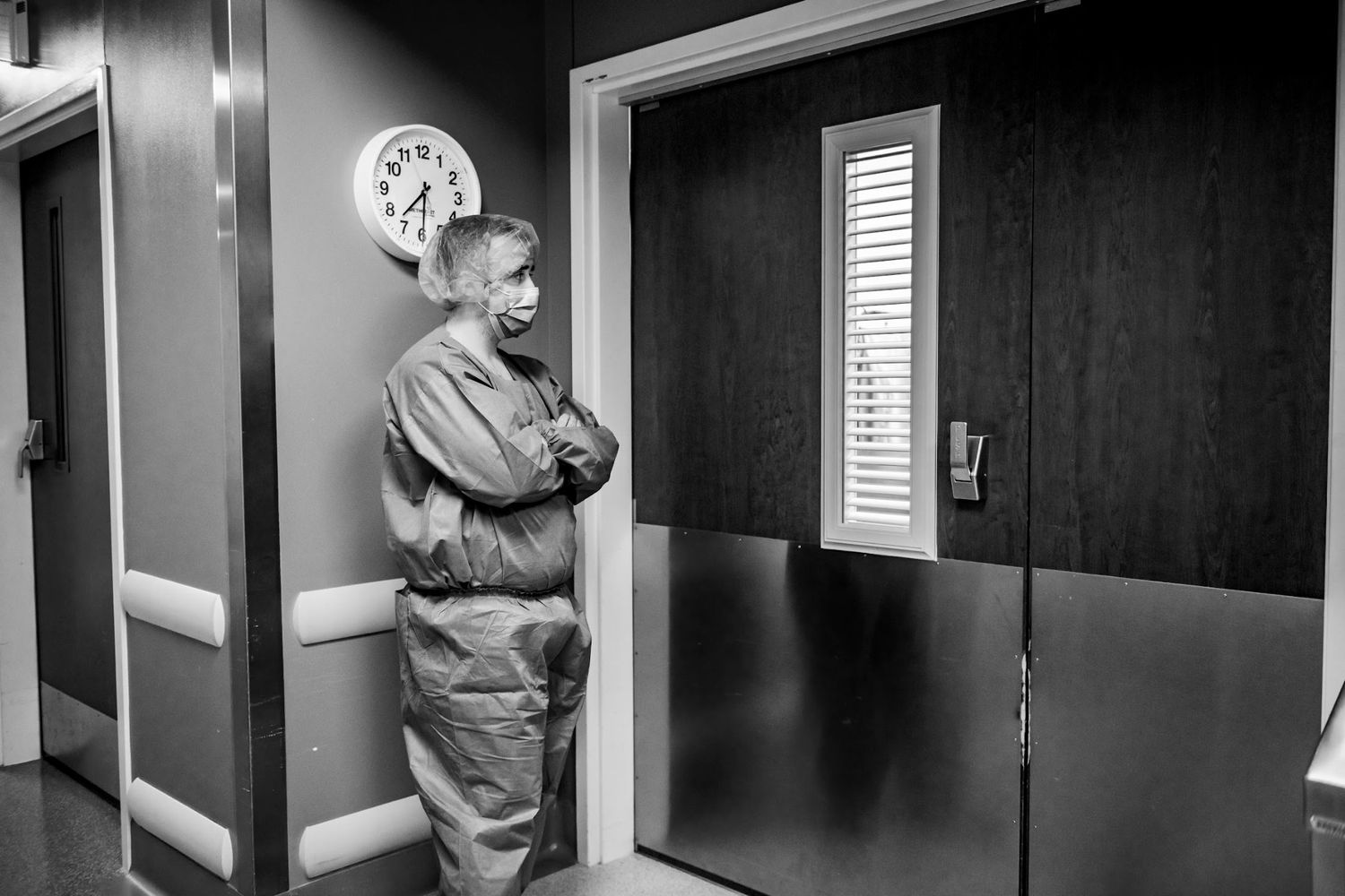 dad in protective gear stands in hospital hallway near OR doorway.