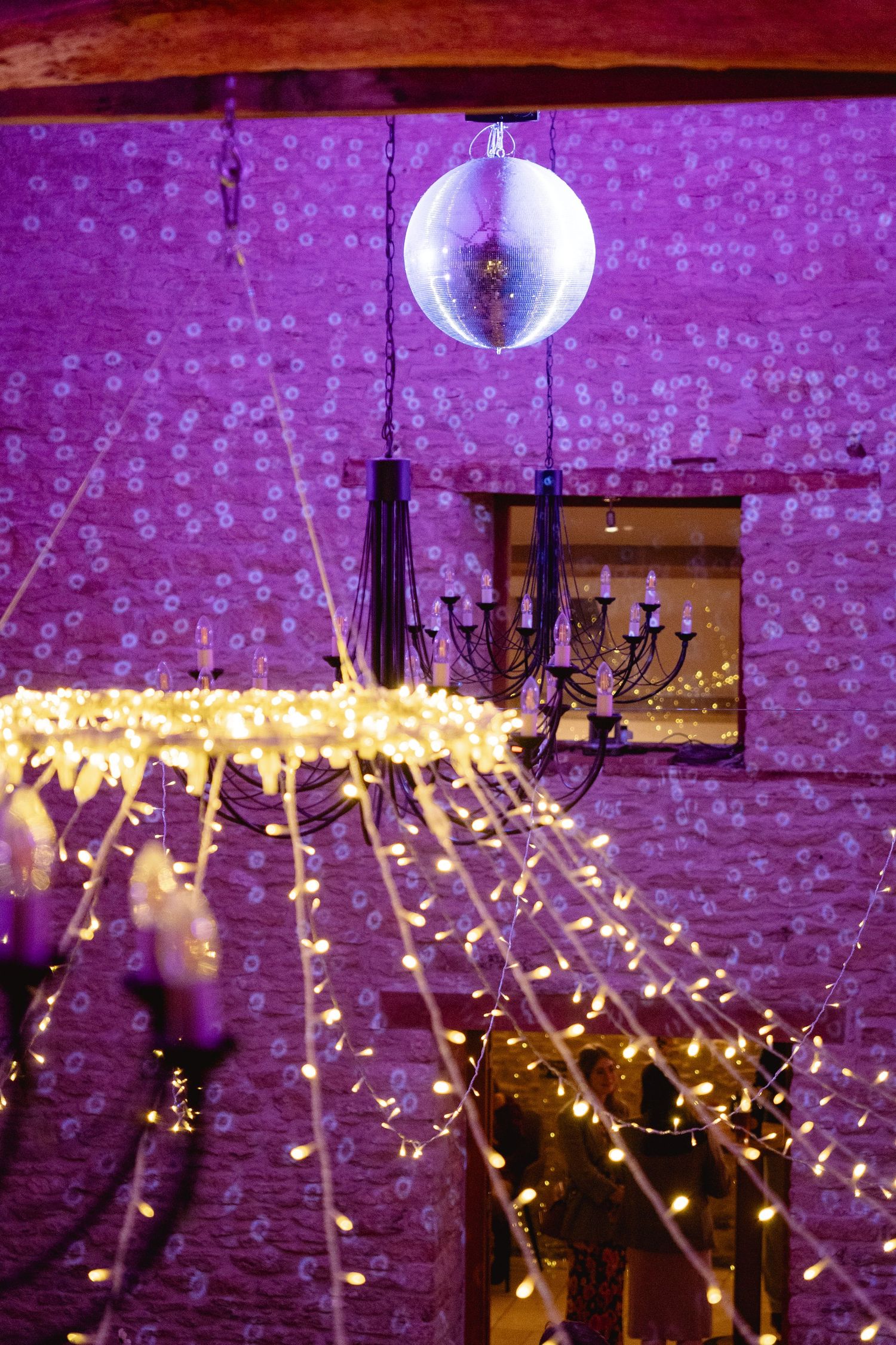 Disco ball and fairy lights illuminate a purple-lit barn venue with black candelabras for a magical event.