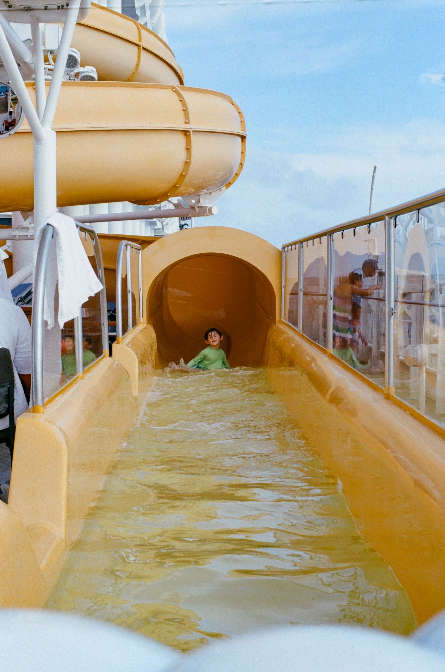 Child sliding down a yellow water slide on a cruise ship deck on a sunny day.