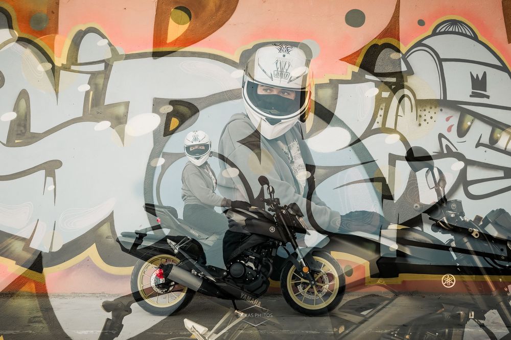 Motorcyclist in white helmet poses on a naked bike in front of vibrant graffiti wall art mural.