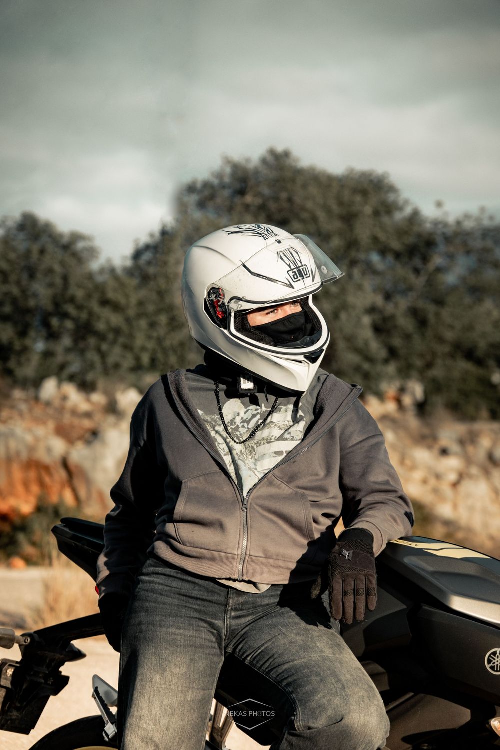 Motorcyclist wearing a white full-face helmet and gray hoodie sitting on a bike outdoors.