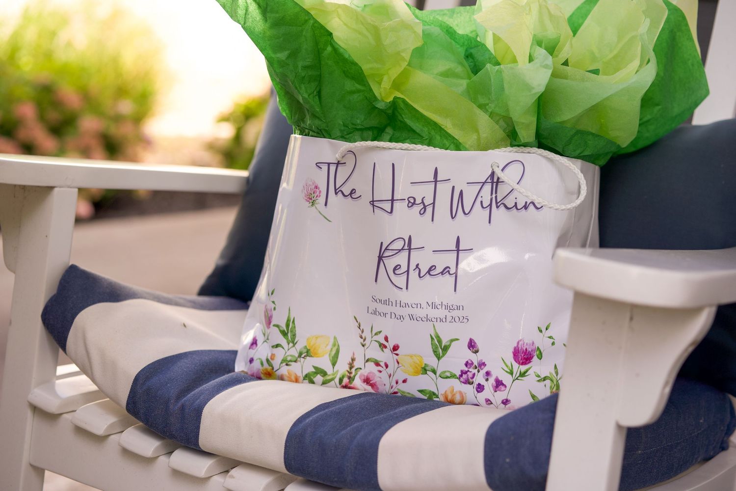 A gift bag for The Host Within Retreat sits on a navy striped Adirondack chair with green tissue paper.