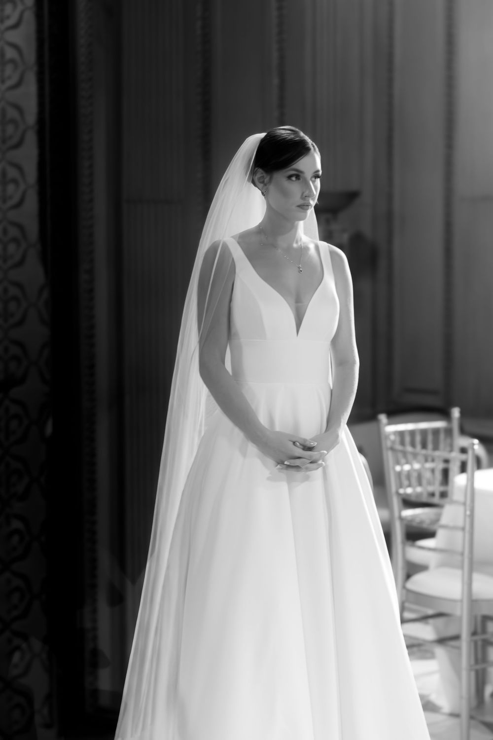 Elegant bride in a classic white ball gown and veil poses gracefully in a black and white wedding photo.