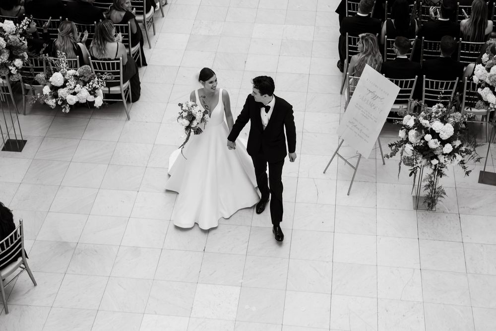 Aerial black and white photo of bride and groom walking hand in hand at wedding reception.