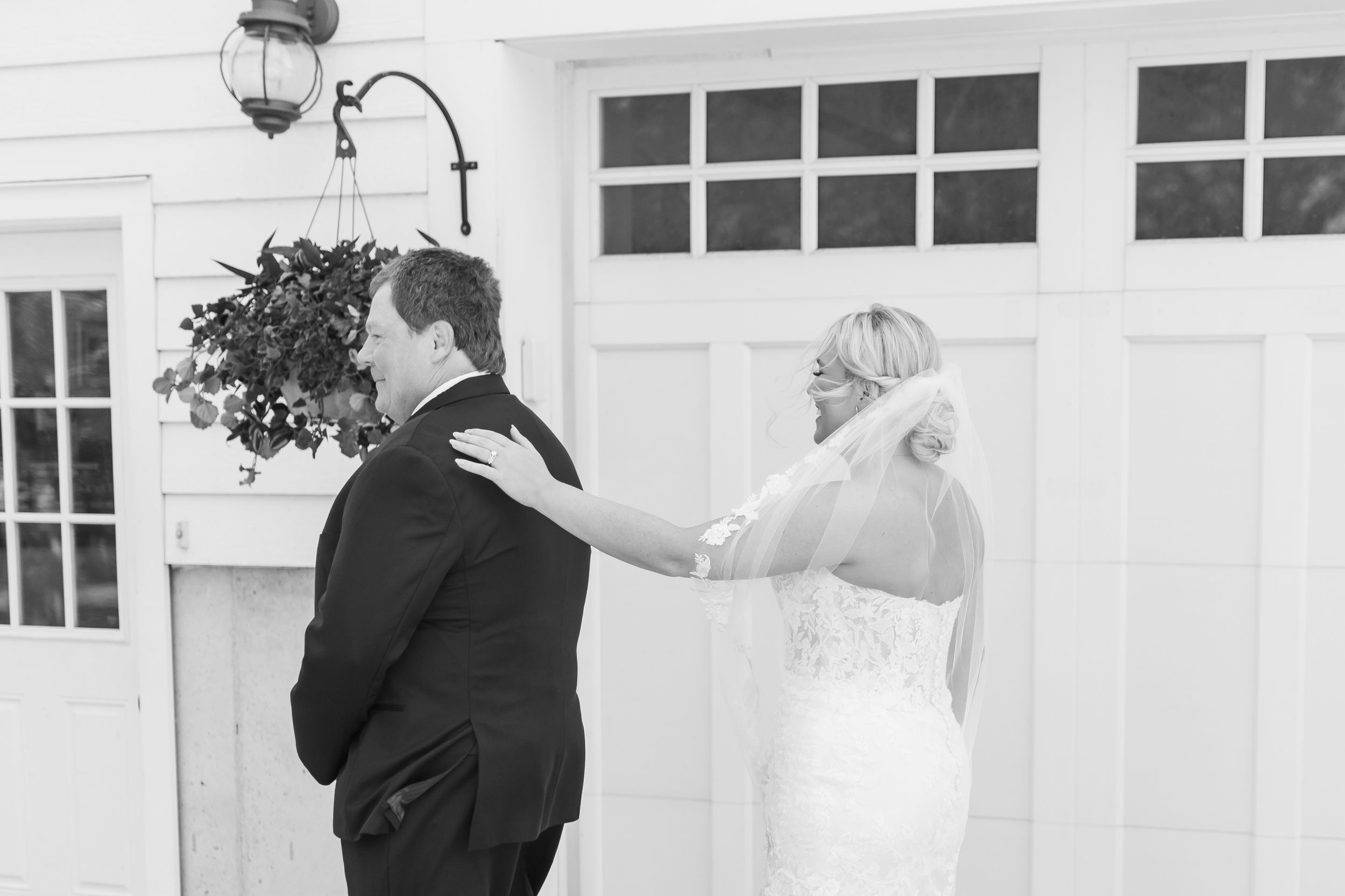 Black and white photo of a bride and groom sharing a first look moment outside a white barn on their wedding day.