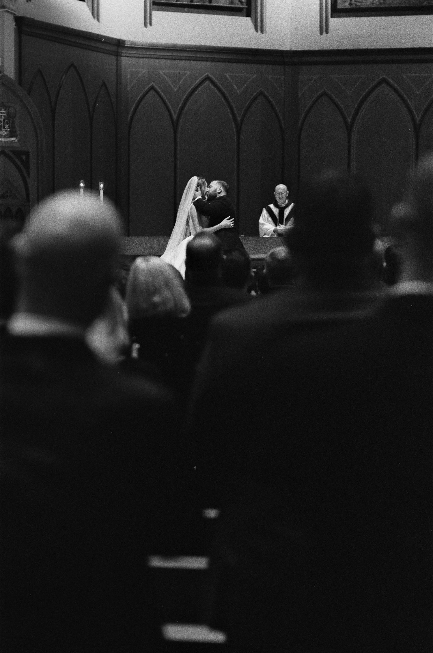 35mm film photo of a couple sharing their first kiss at a church wedding ceremony with guests watching.