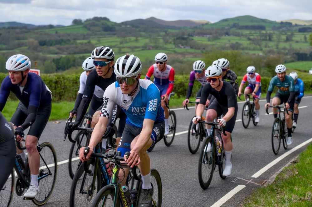 Cyclists competing in a road race through scenic green countryside, wearing colorful jerseys and helmets on a rural road.