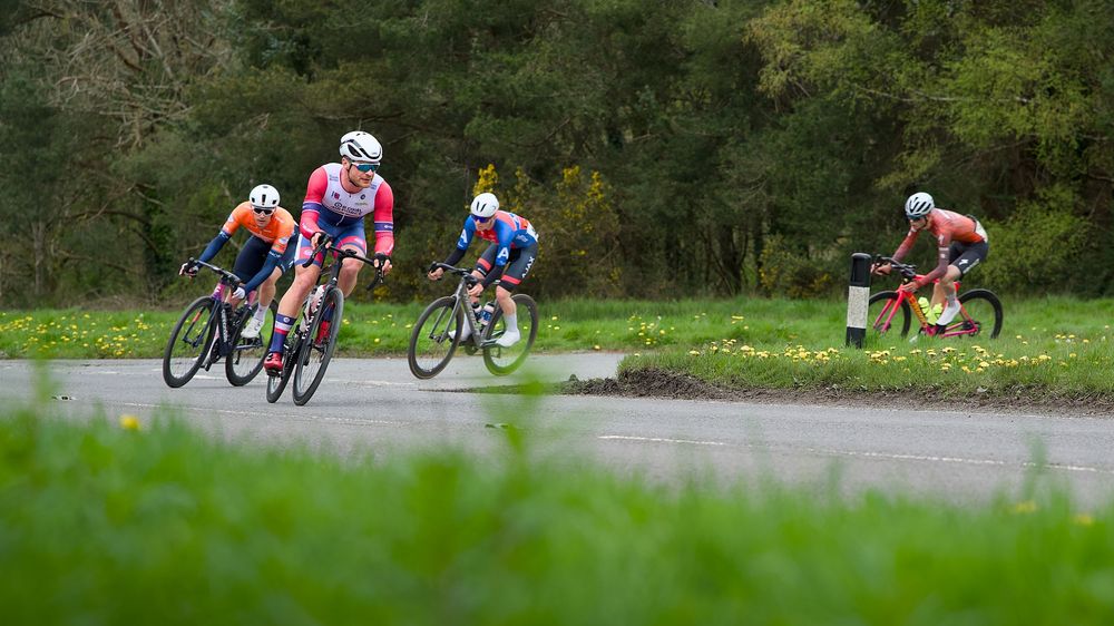 Group of five cyclists competing in a road race through a scenic green countryside on a cloudy day.