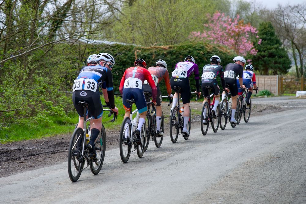 Group of cyclists racing on a rural road during a competitive cycling event, surrounded by spring trees and greenery.
